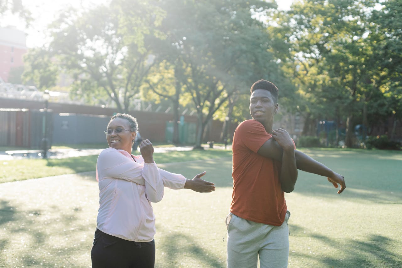 Two diverse adults stretching in a sunny park, embracing a healthy lifestyle.